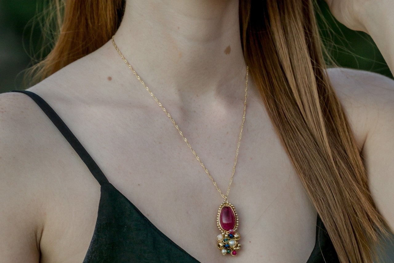 Woman with long hair wearing ruby gem pendant on yellow gold chain