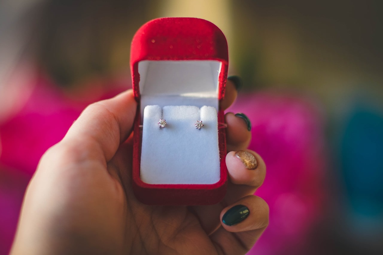 A close-up of a pair of diamond stud earrings inside an open red jewelry box