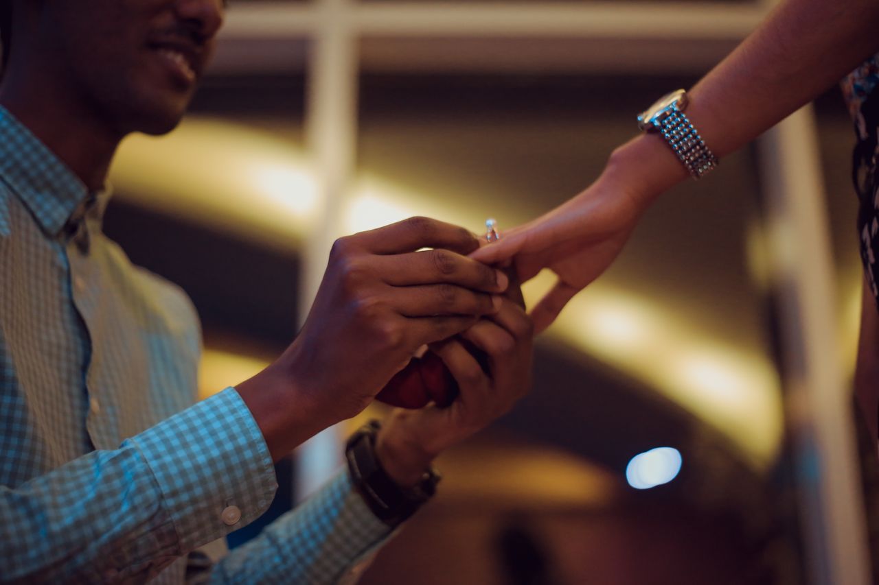 A man putting an engagement ring on a woman’s finger after getting down on one knee and proposing