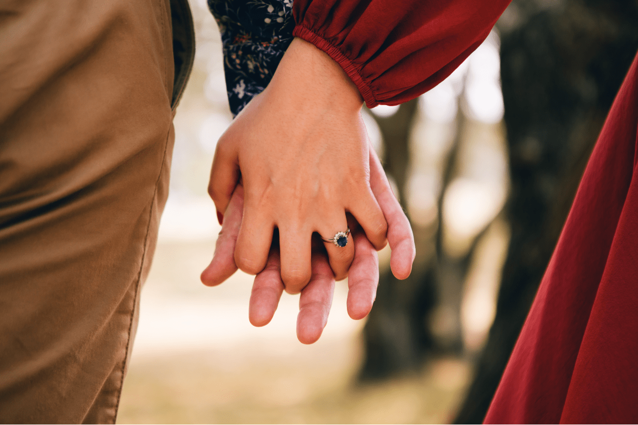 A sapphire and halo engagement ring on the hand of a woman holding the hand of her love