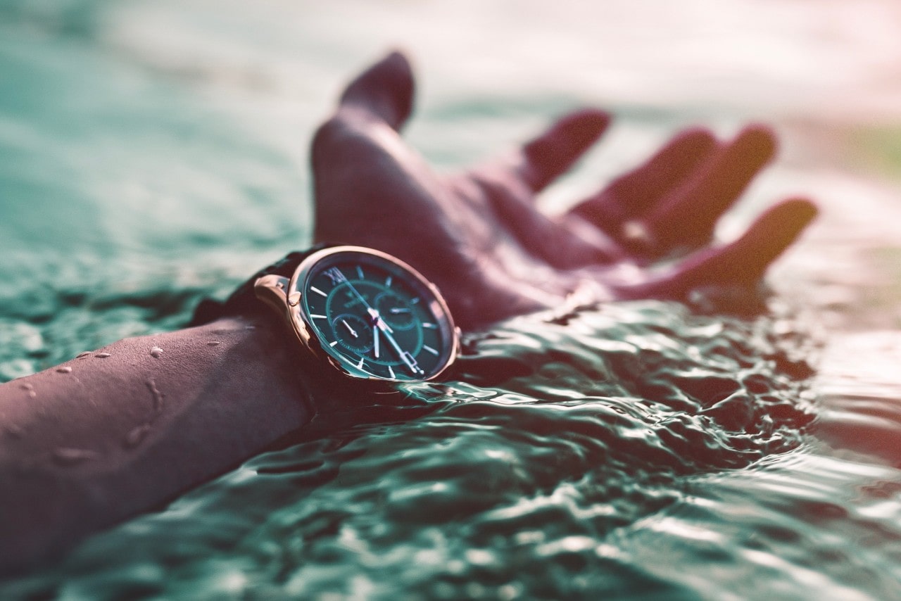 An upturned hand in the water, wearing a black and gold sports watch