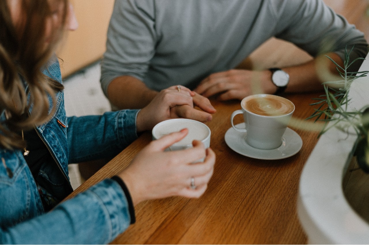 An engaged couple holds hands in a coffee shop