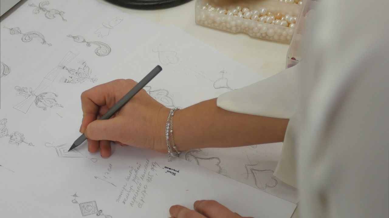 A jewelry designer sketches out a new design at her workstation
