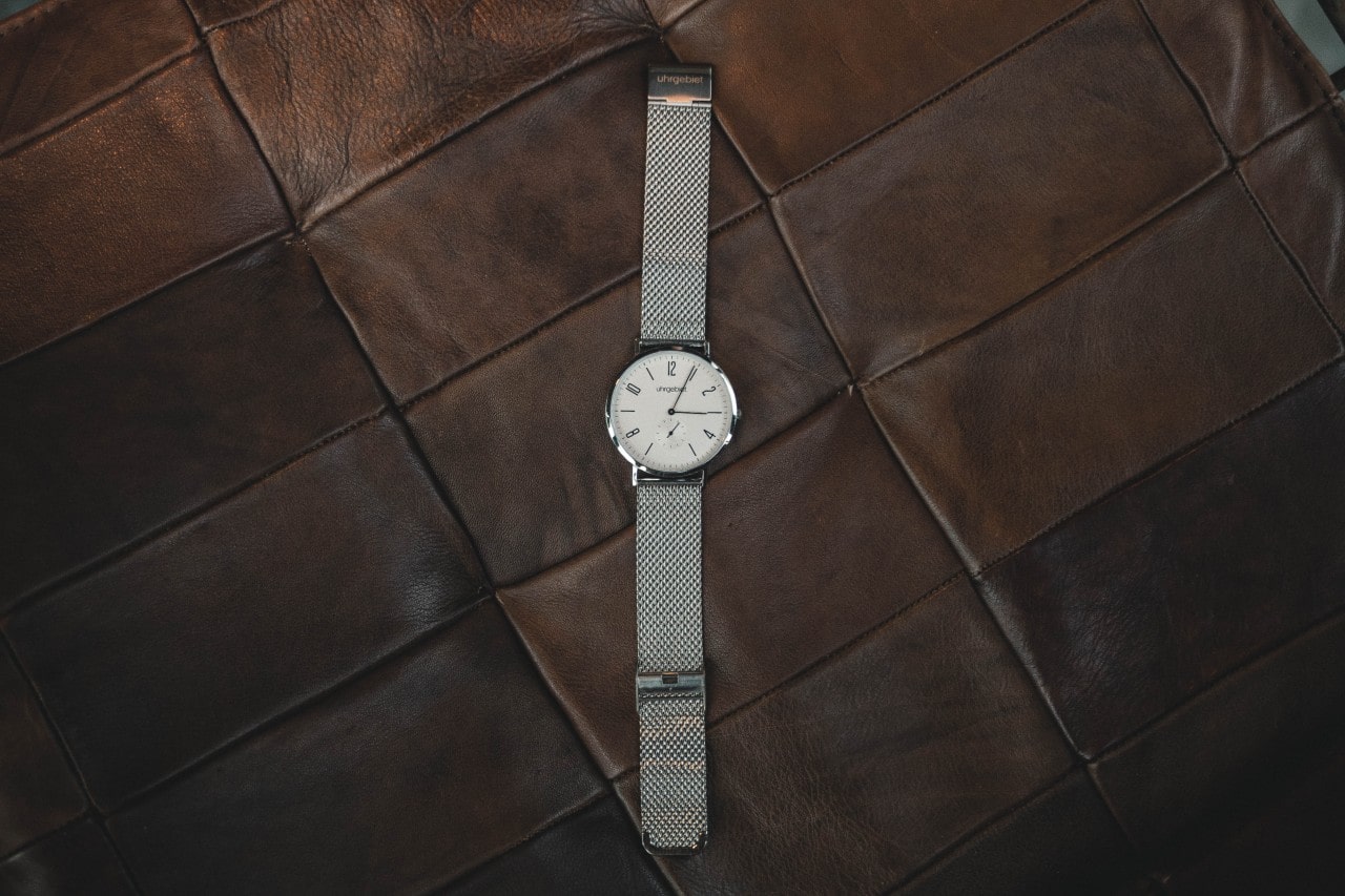 A silver and white minimalist timepiece sits on a brown leather couch