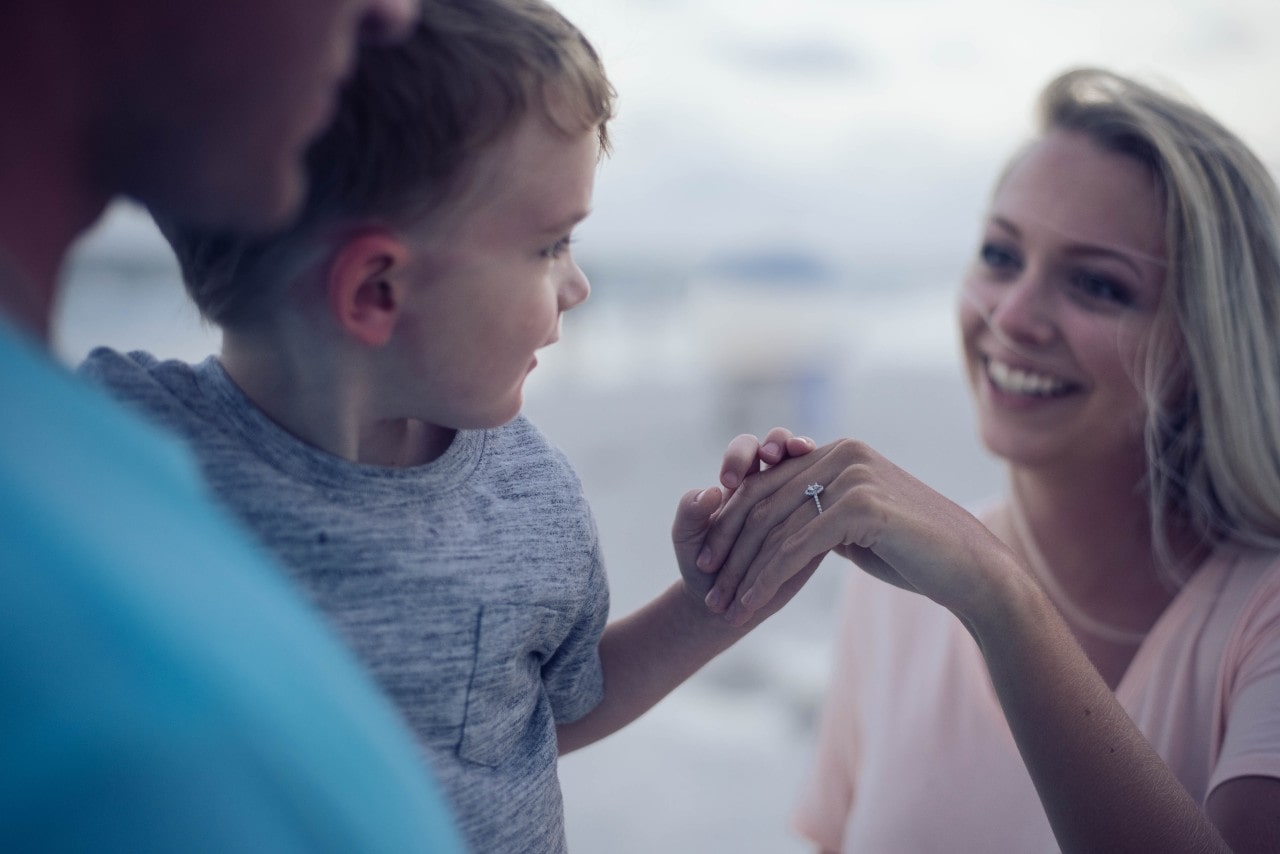 A woman shows her engagement ring to her young son while outside
