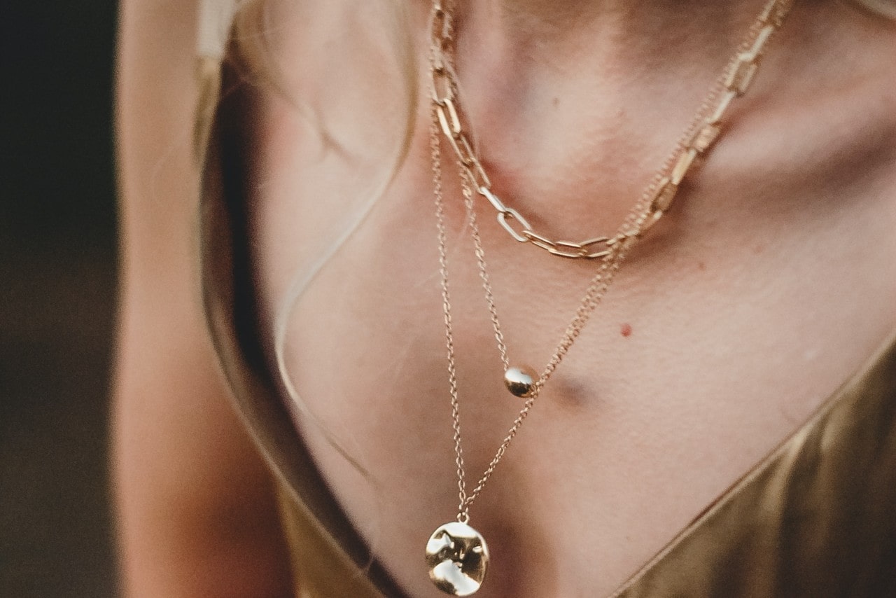 A woman’s neckline wearing three gold necklaces of different lengths