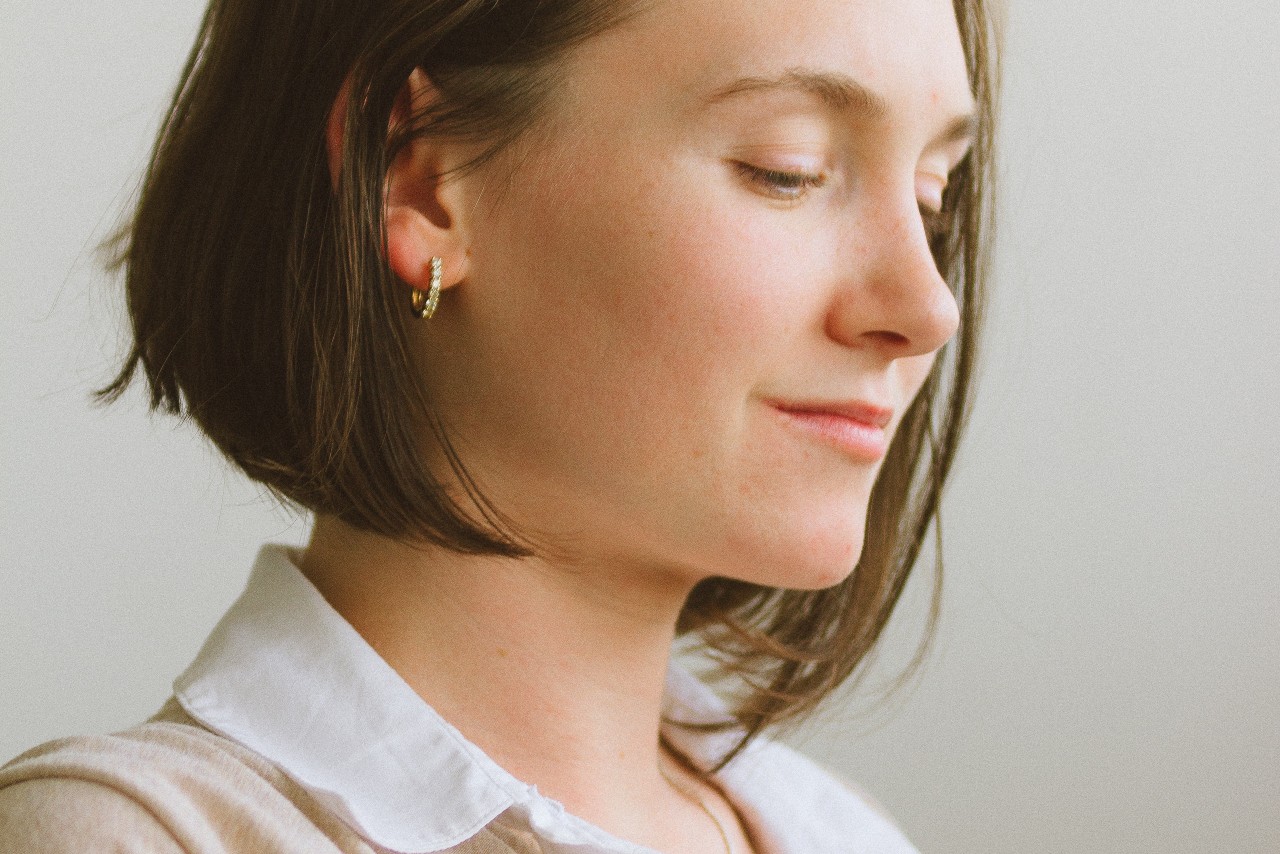 A woman wearing a collared shirt and a small pair of gold huggie earrings