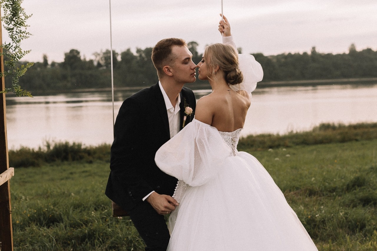 A bride and groom sitting together on a swing in front of a lake