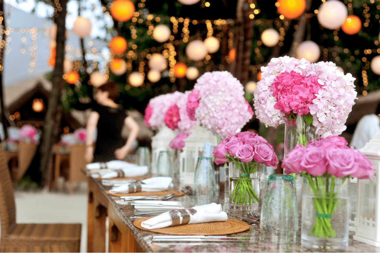A table set at a wedding reception with pink flowers and lights in the background