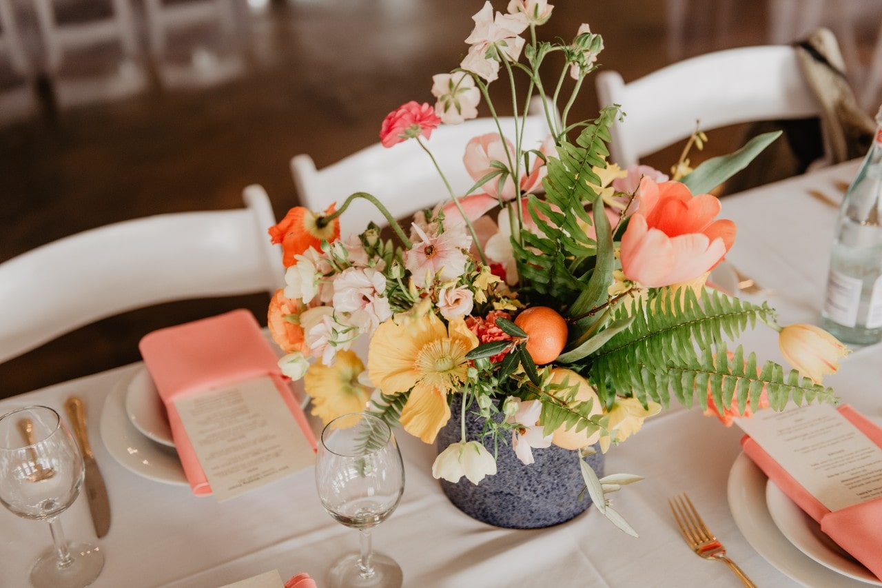 A table set at a wedding reception with a peachy color scheme and colorful centerpiece
