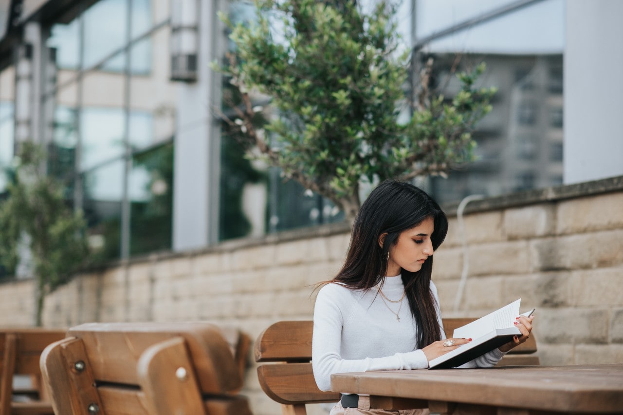 Woman sitting at a table outside and reading a book