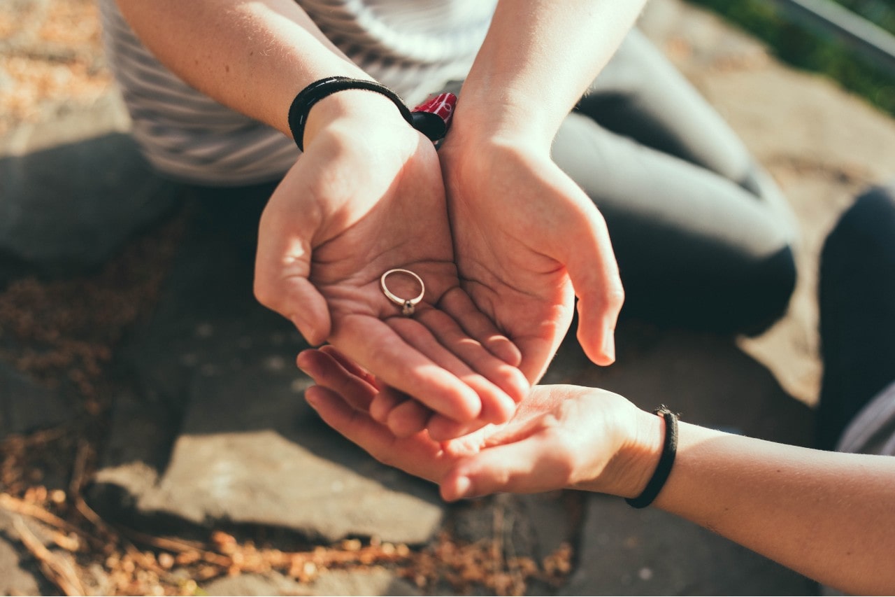 A man holds an engagement ring in his palm while sitting outside.