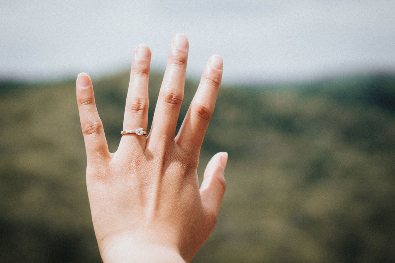 A woman admires her solitaire engagement ring outside.