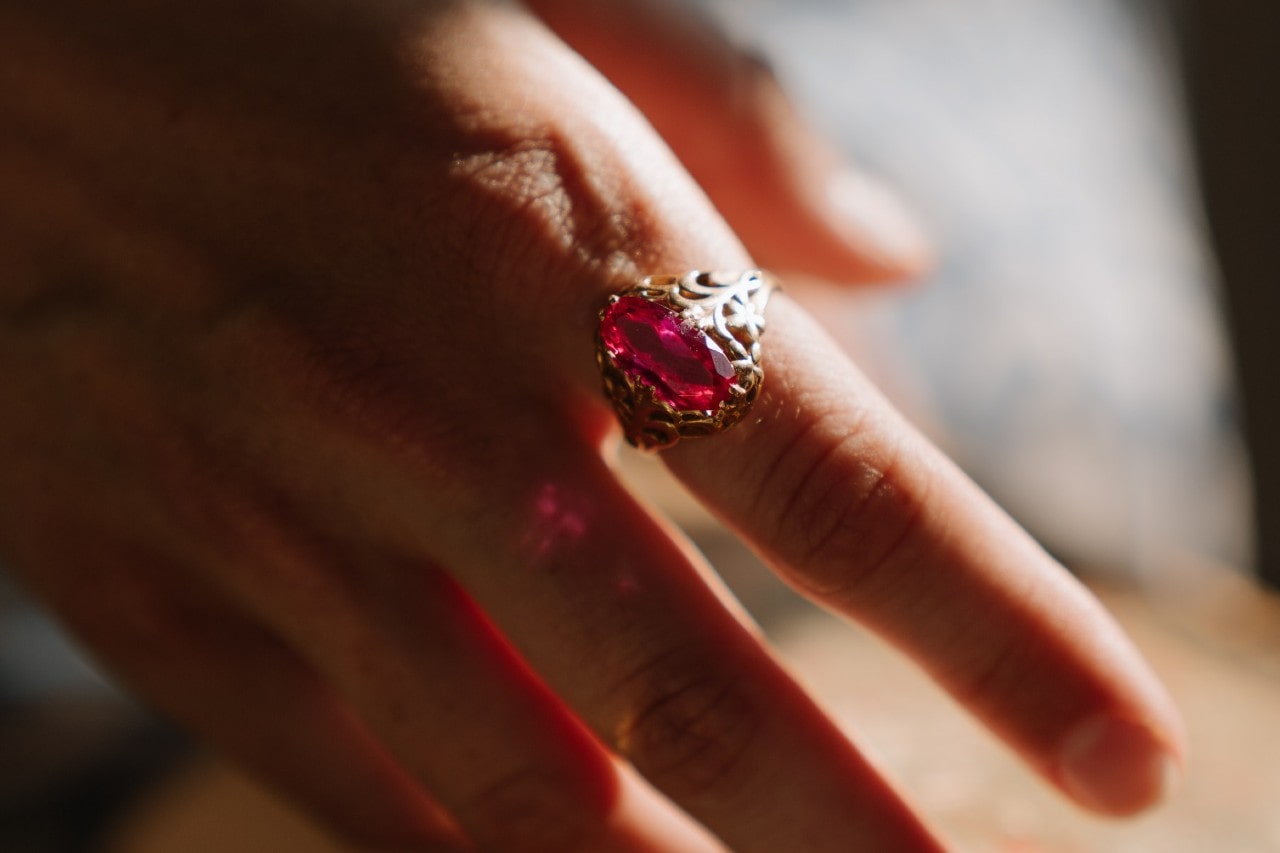 close up image of a hand wearing an elaborate fashion ring featuring a red gem