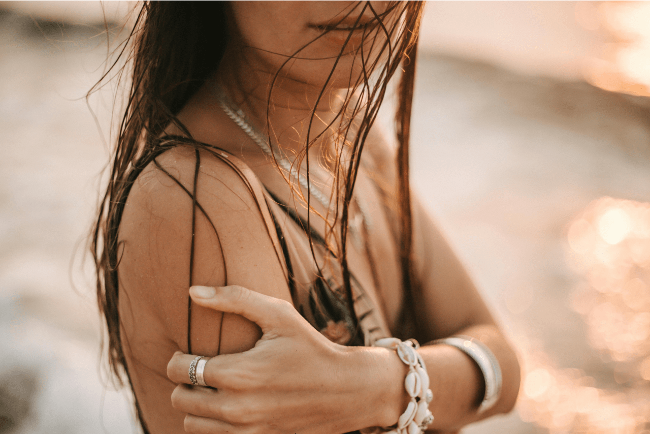 A close-up of a woman with wet hair on the beach wearing silver and shell jewelry.