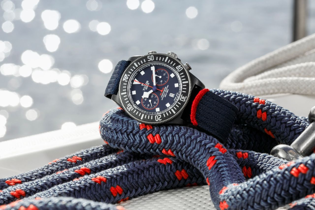 close up of a TUDOR Pelagos watch with navy and red nautical details, a black bezel, and chronometer all on a comfortable nylon watch strap fits in perfectly with boat lines on a dock.
