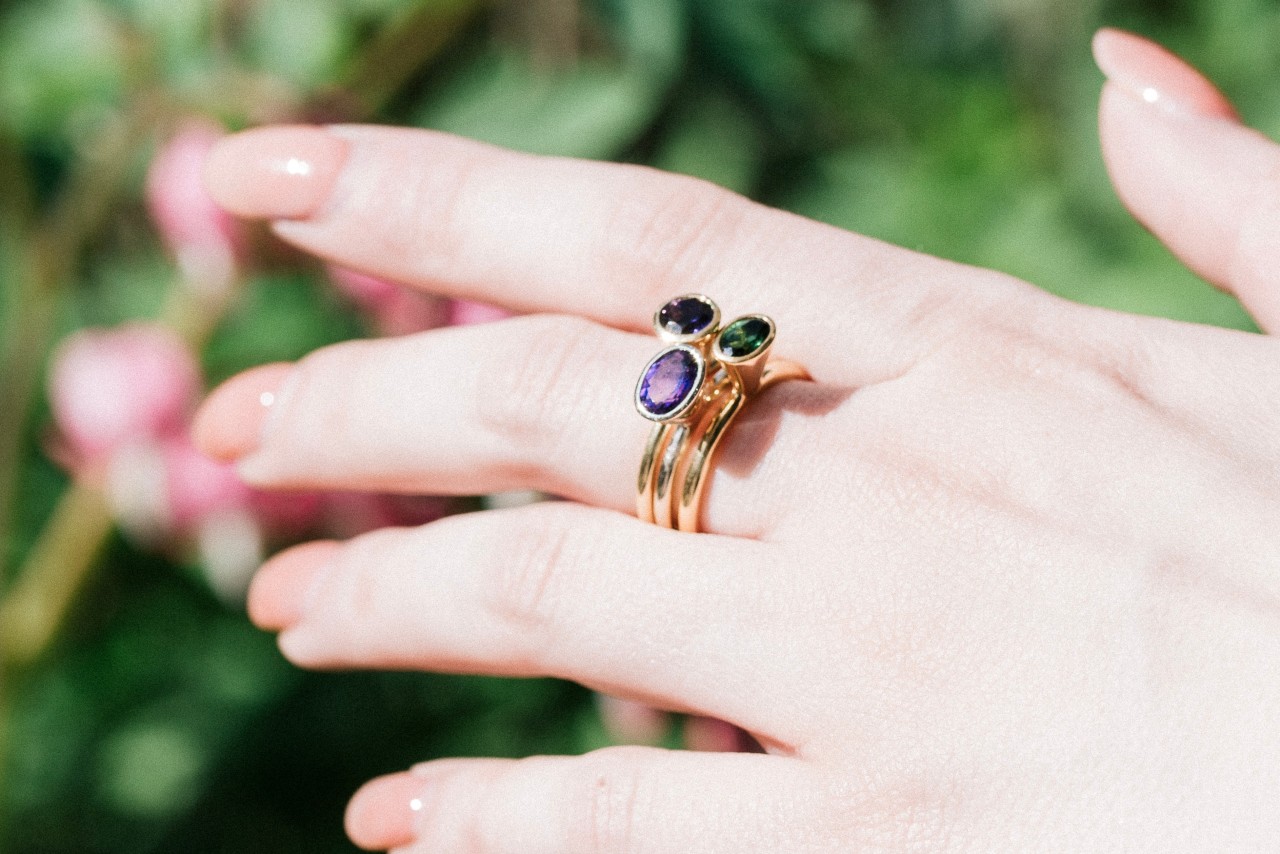 an outstretched hand donning three stacked fashion rings featuring different gemstones