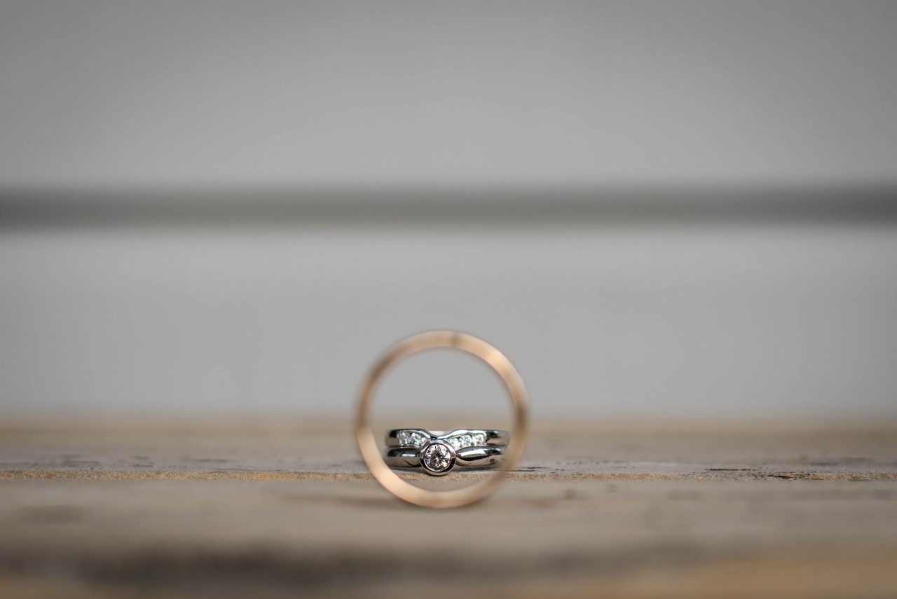 an image of a white gold engagement ring and wedding band seen through the middle of a blurred gold wedding band