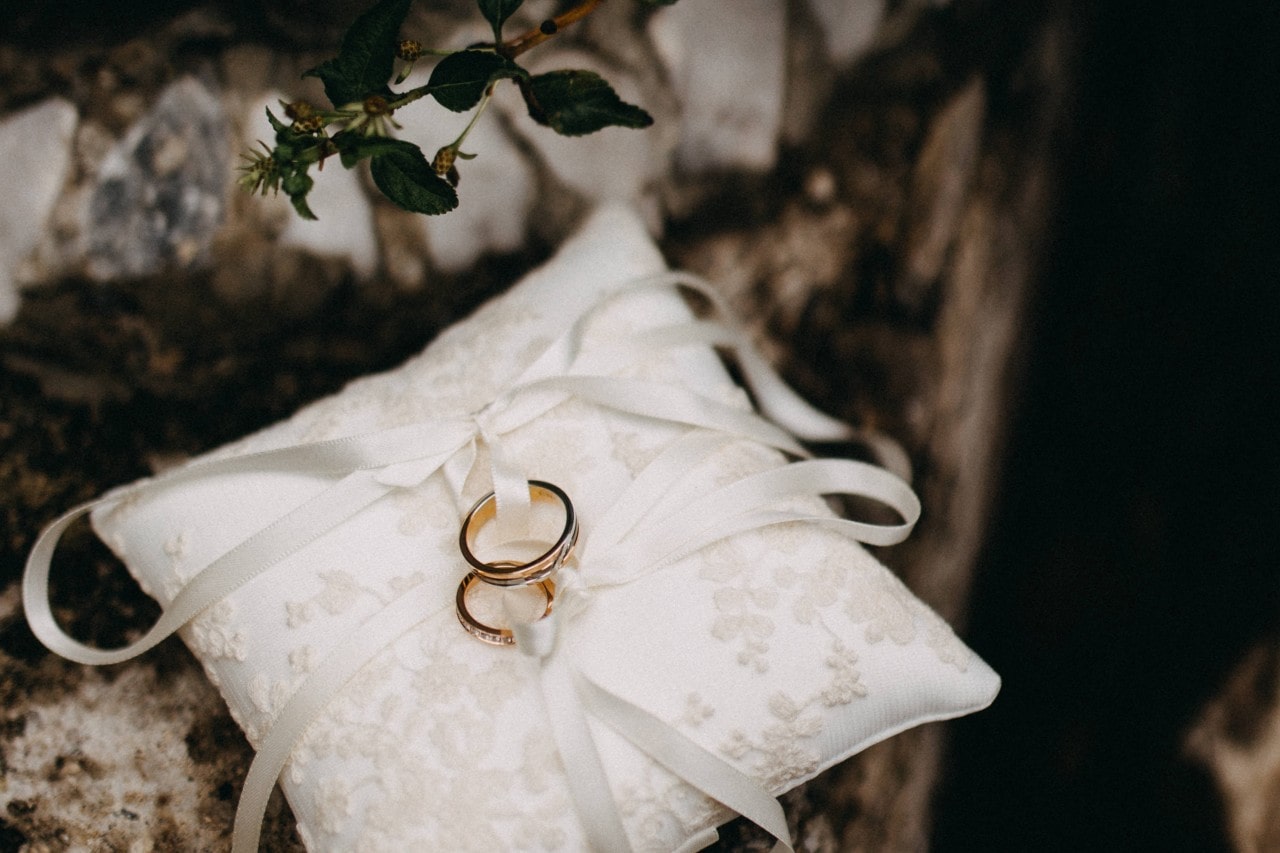 a pair of wedding bands tied with white ribbon to a small white pillow
