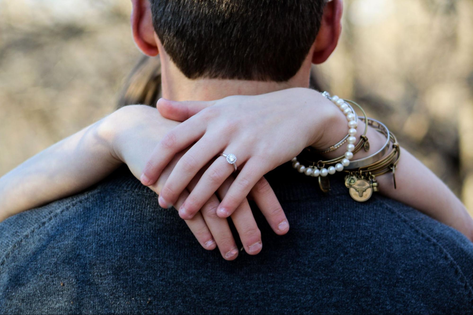 A woman wraps her arms around her partner’s neck, wearing a variety of bracelets.