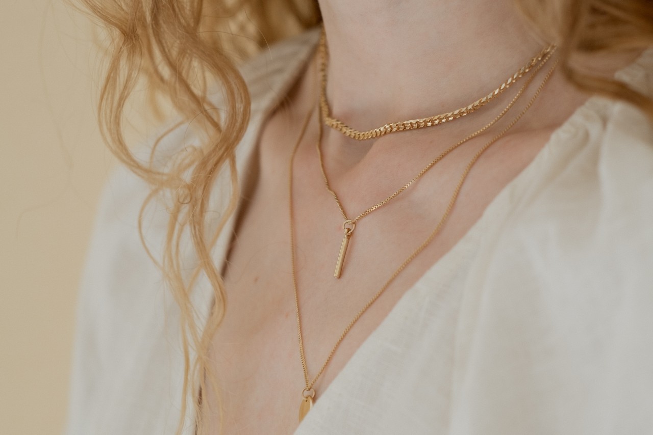 A woman’s neckline showcasing three layered gold necklaces.