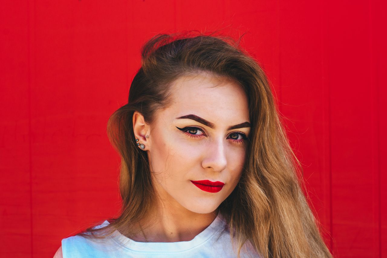 A woman in front of a red wall wears multiple white gold stud earrings.