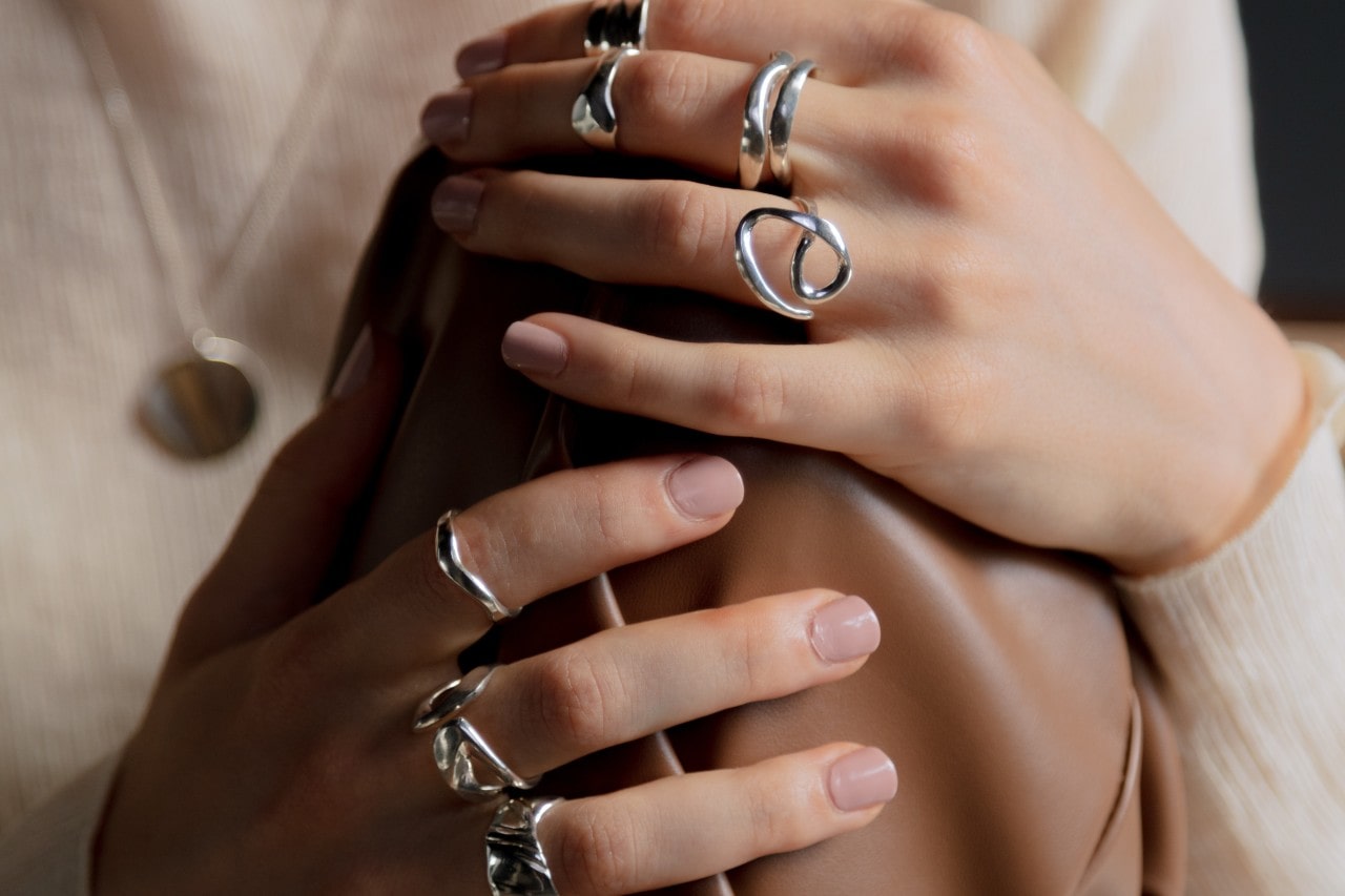 A woman holding a leather bag wears multiple white gold rings.