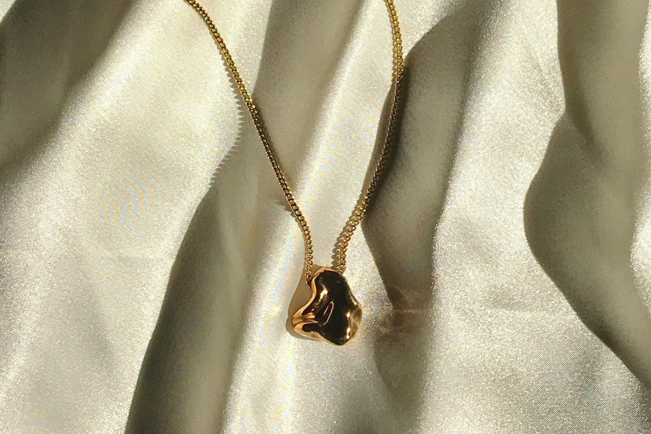 A yellow gold pendant necklace with a sculptural pendant displayed atop soft, beige fabric.