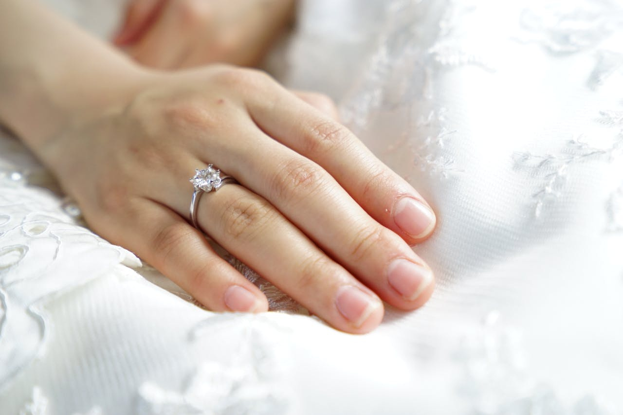 A close up of a bride&rsquo;s hand laying on top of the white fabric, showcasing white gold diamond engagement ring.