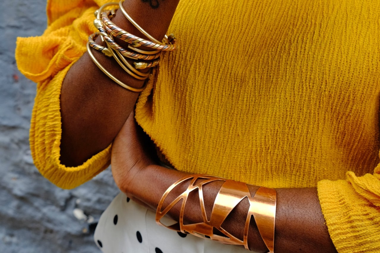 A close-up of a fashionably dressed woman’s forearms, both adorned with distinctive, sculptural bracelets.