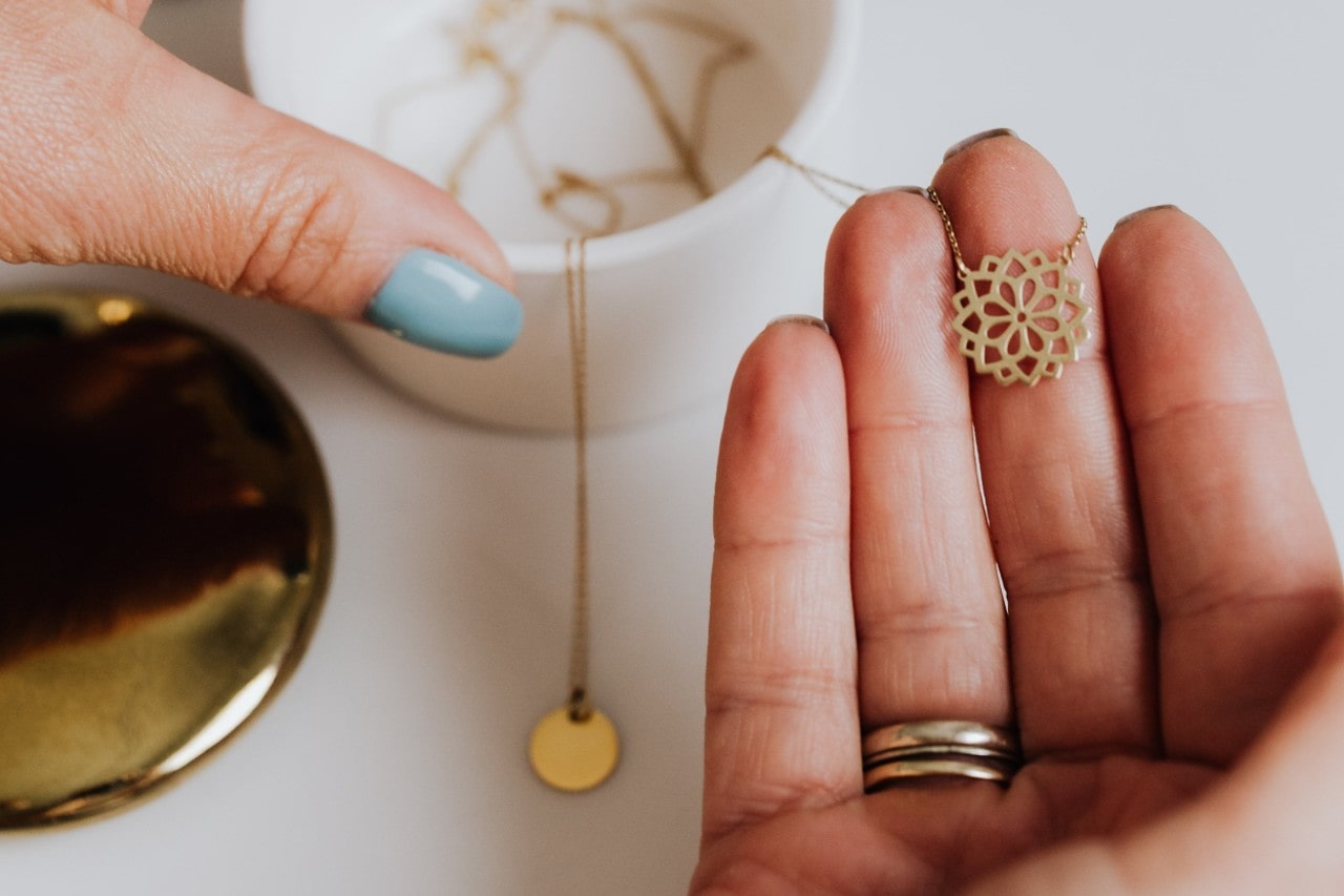 a woman’s hand holding a yellow gold pendant necklace with a floral motif