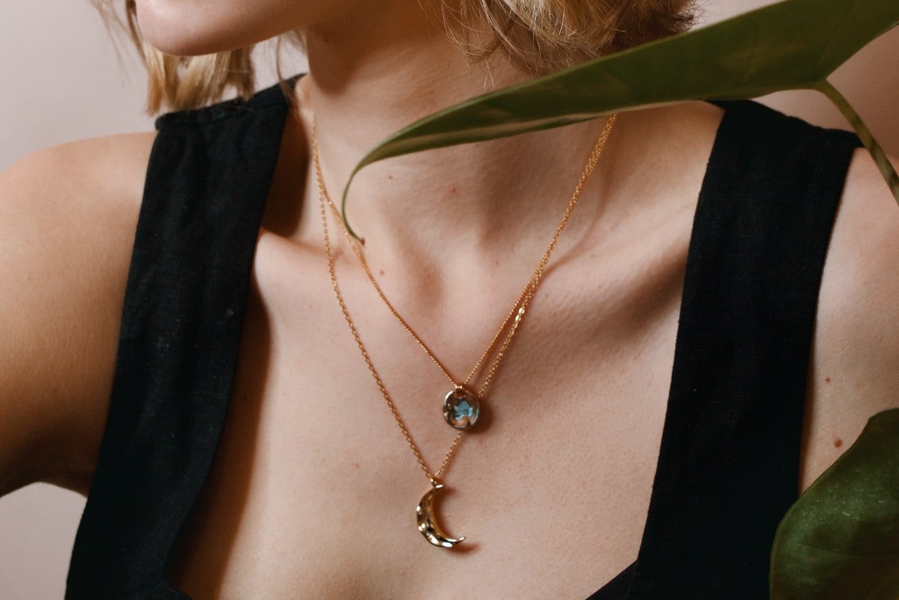 close up image of a woman’s neckline wearing two yellow gold pendant necklaces