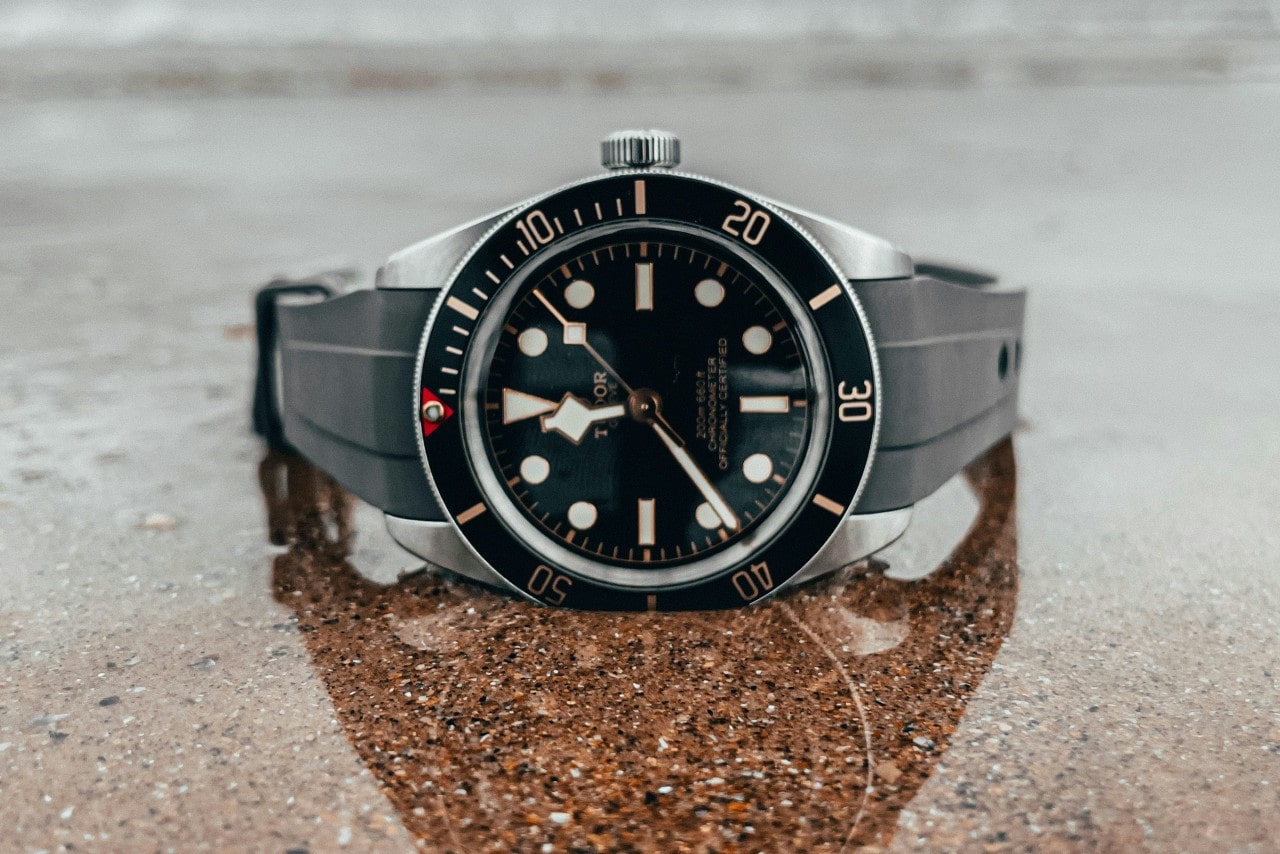 A close-up of a TUDOR sports watch displayed on its side on a reflective granite surface.