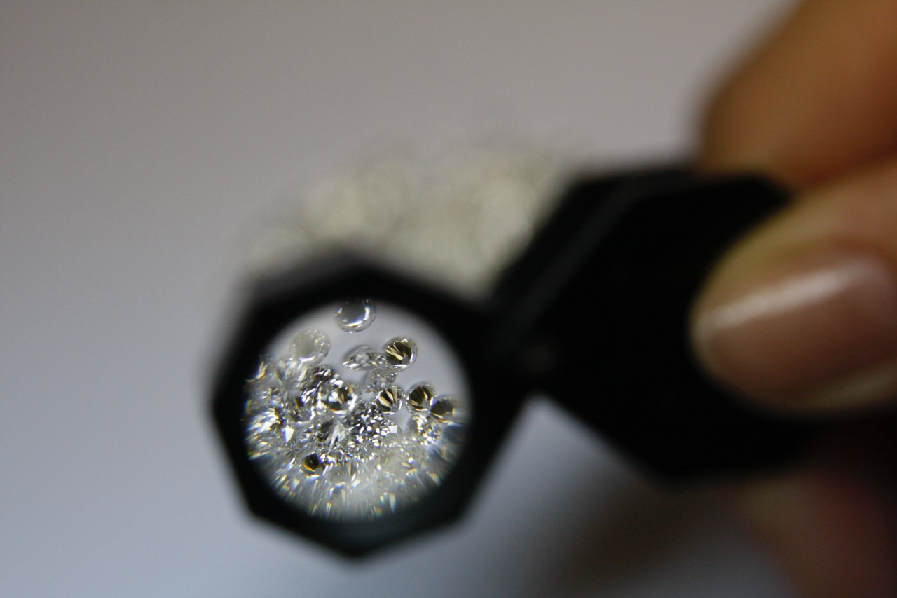 a magnifying glass held up to a pile of small round cut diamonds