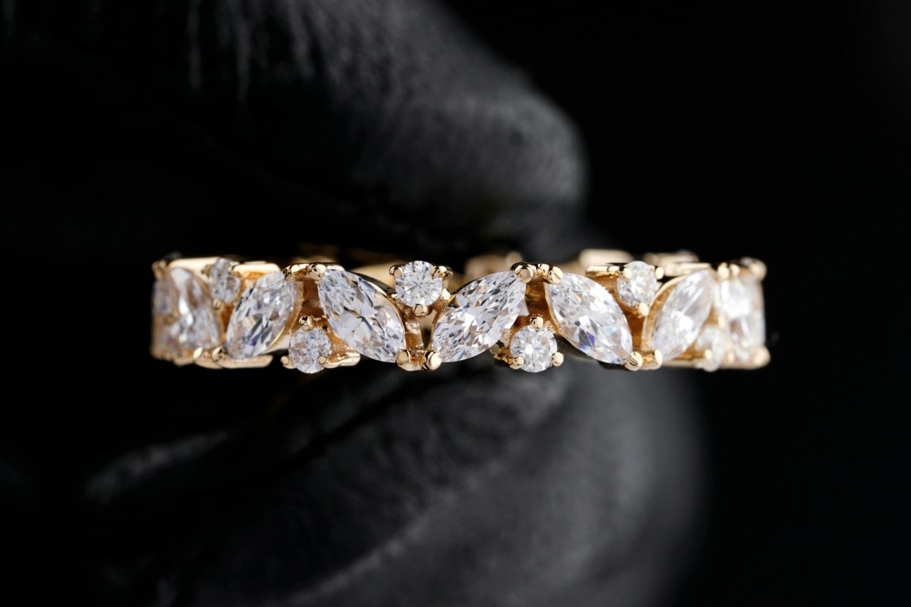 A close-up of a stunning yellow gold wedding band adorned with round and marquise cut diamonds, held carefully on a black leather backdrop.