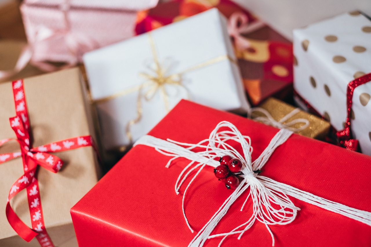 A close-up of multiple festive holiday gifts, with a red gift box tied with white string and adorned with holly berries at the front.