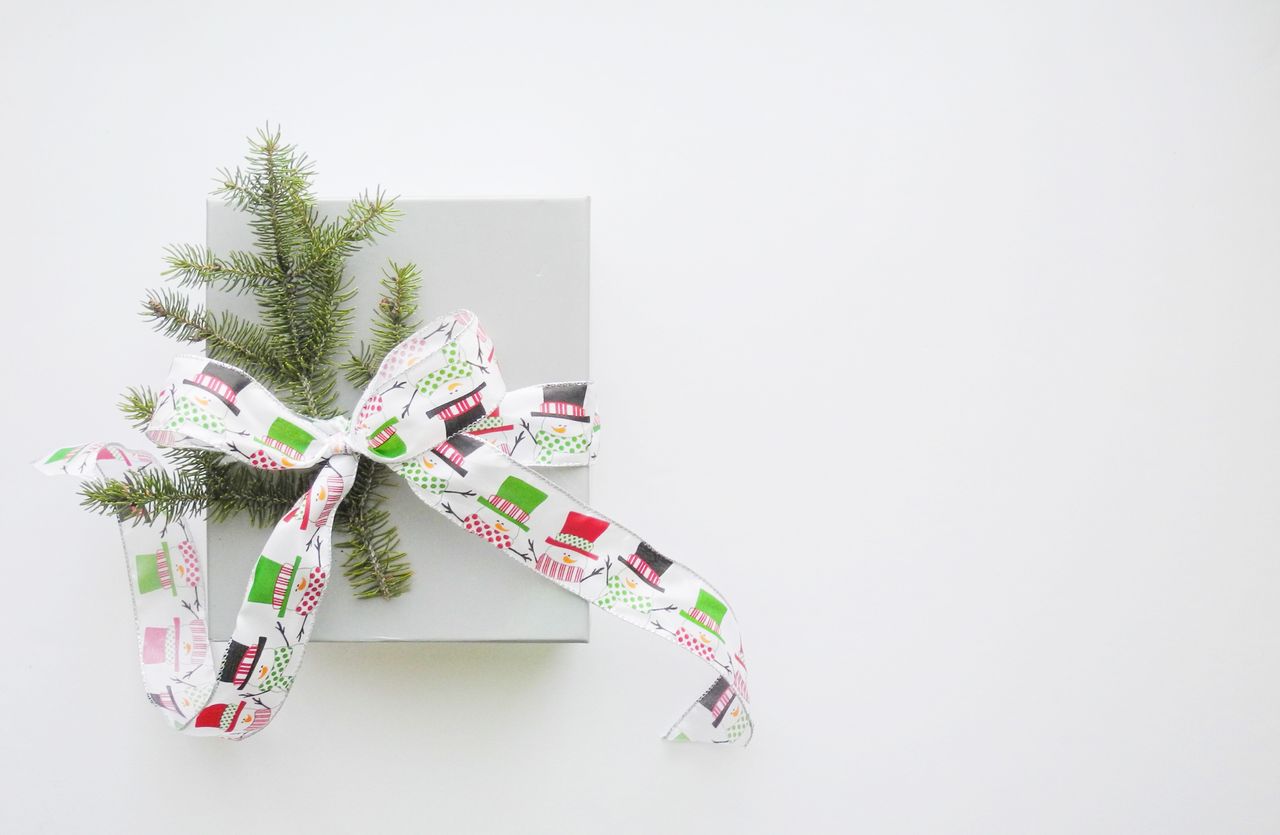 A close-up of a simple yet elegant gift box decorated with a snowman ribbon and a sprig of pine.