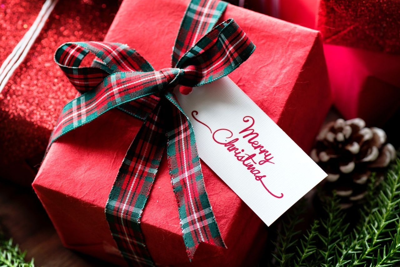 A close-up of a festive Christmas gift wrapped in red paper and a plaid ribbon, with a tag that reads “Merry Christmas.”