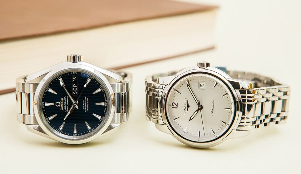 Two wristwatches on a light surface; left with black dial and silver markers showing “SEP 19,” right with white dial and date display.