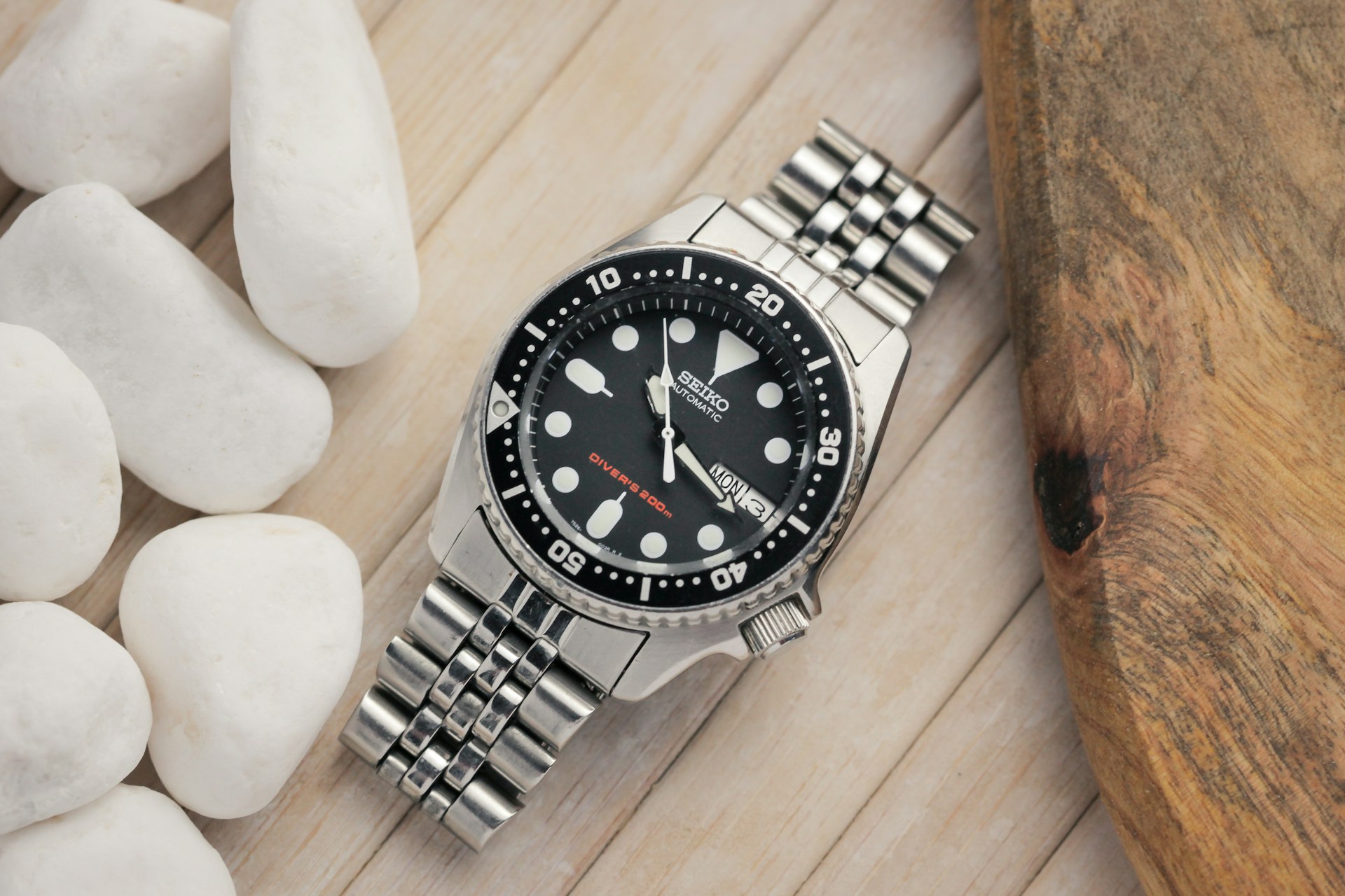 Silver SEIKO watch with a black dial and white markers on a wooden surface, surrounded by white stones.