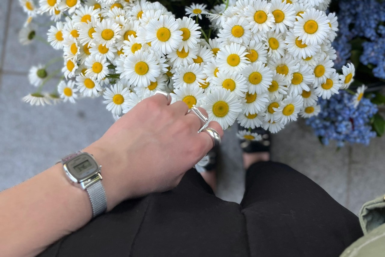 A person’s arm, clad in a casual watch, reaching for a bouquet of daisies.