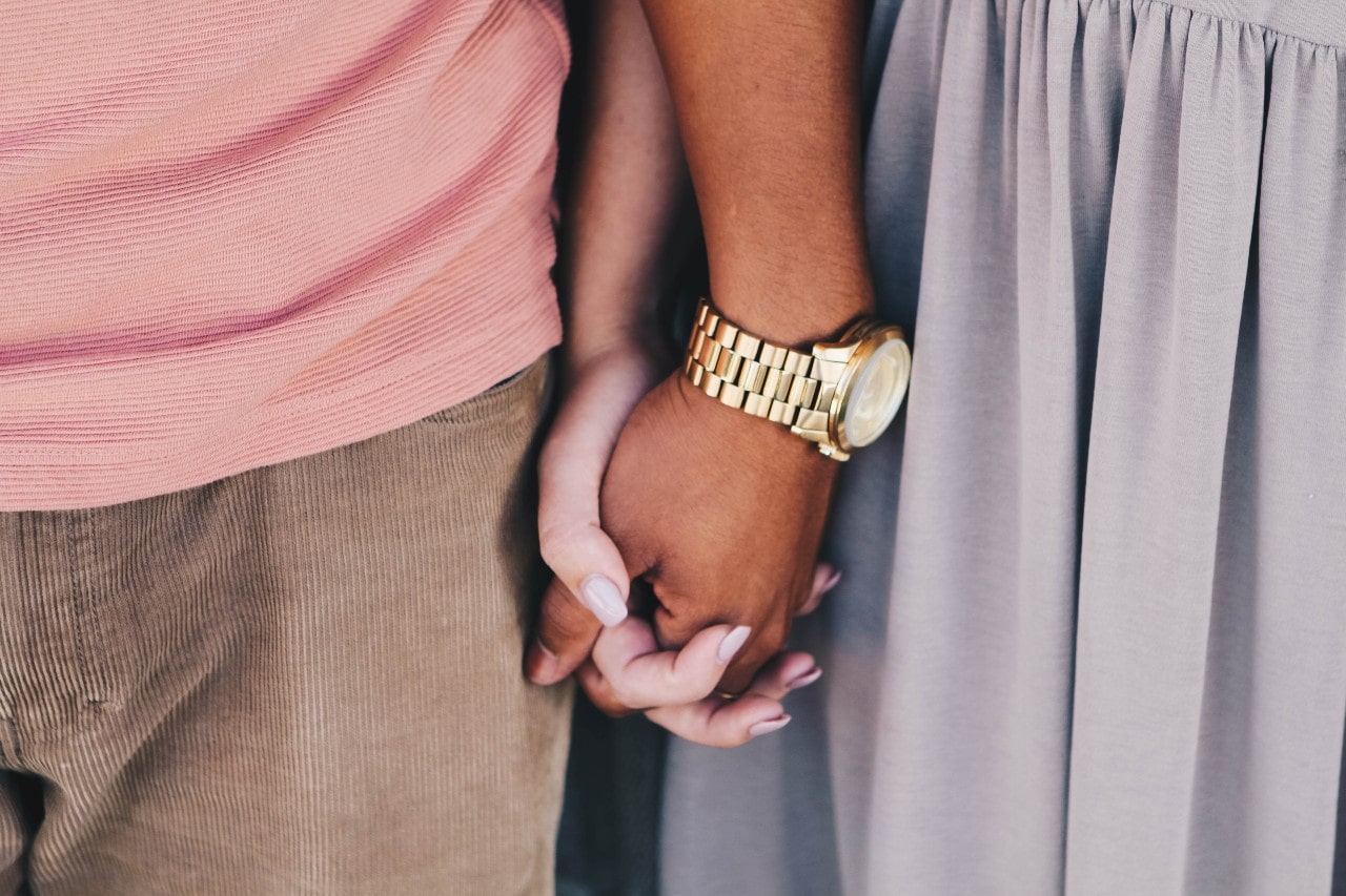 a couple holding hands, the man wearing a yellow gold timepiece
