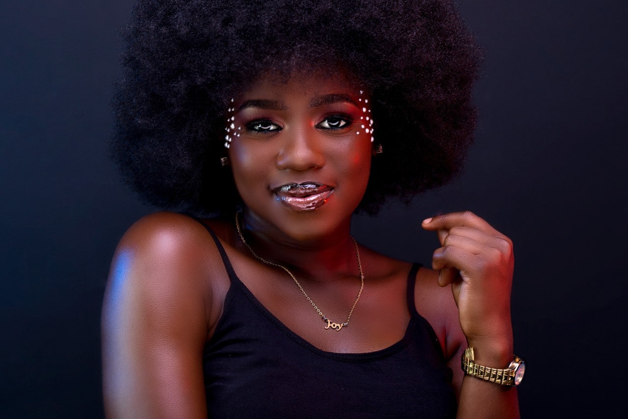 a woman smiling at the camera and wearing a gold watch, gold necklace and jewels on her face