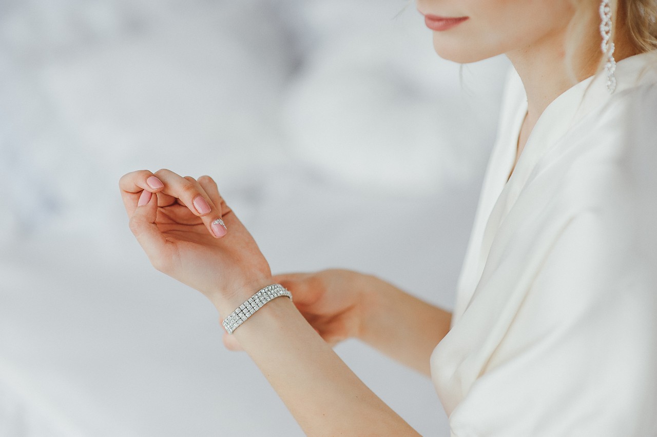 A close up of woman in a white blouse and drop earrings fixing her diamond tennis bracelet.