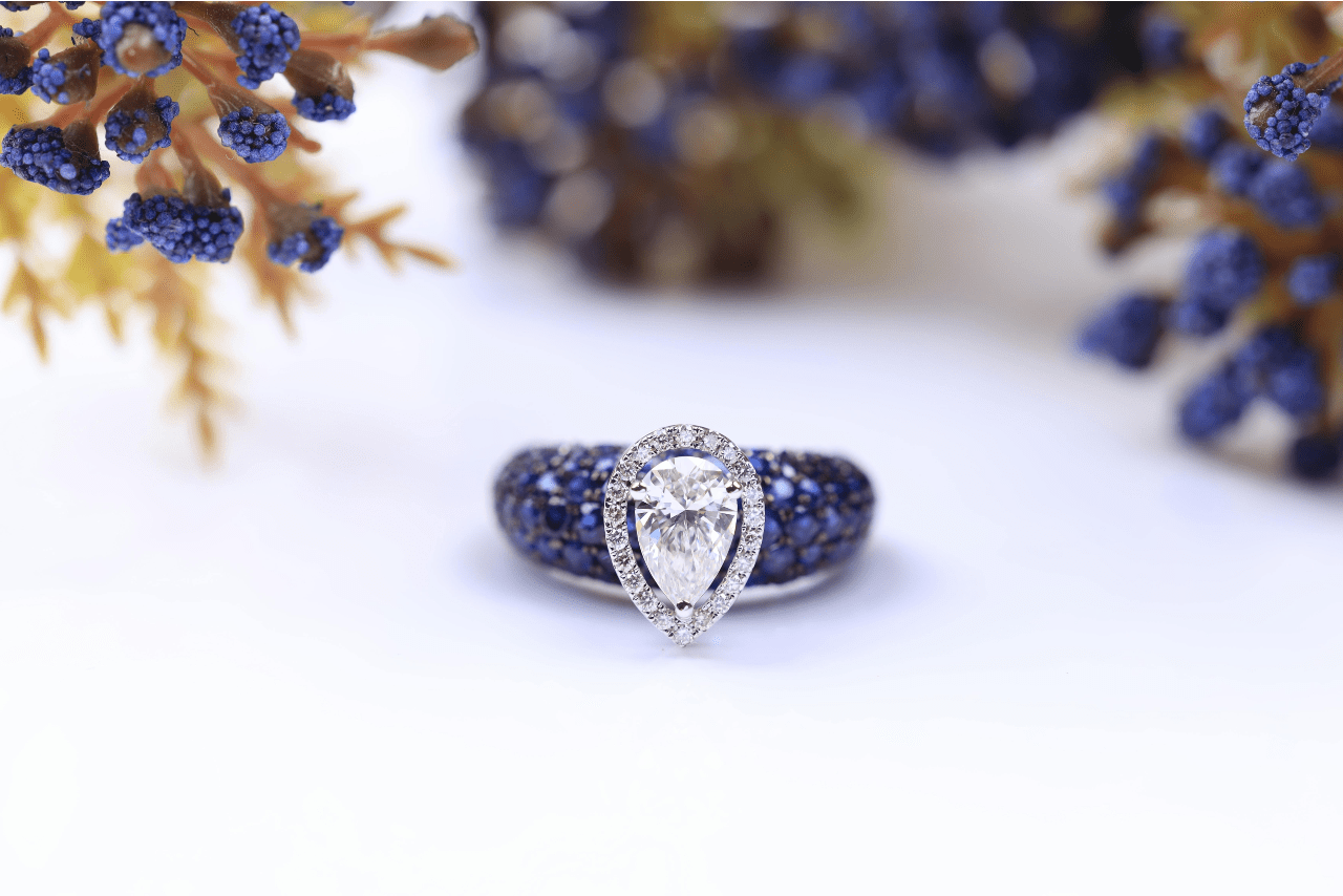 A unique pear shape engagement ring with sapphire side stones displayed among sprigs of juniper.