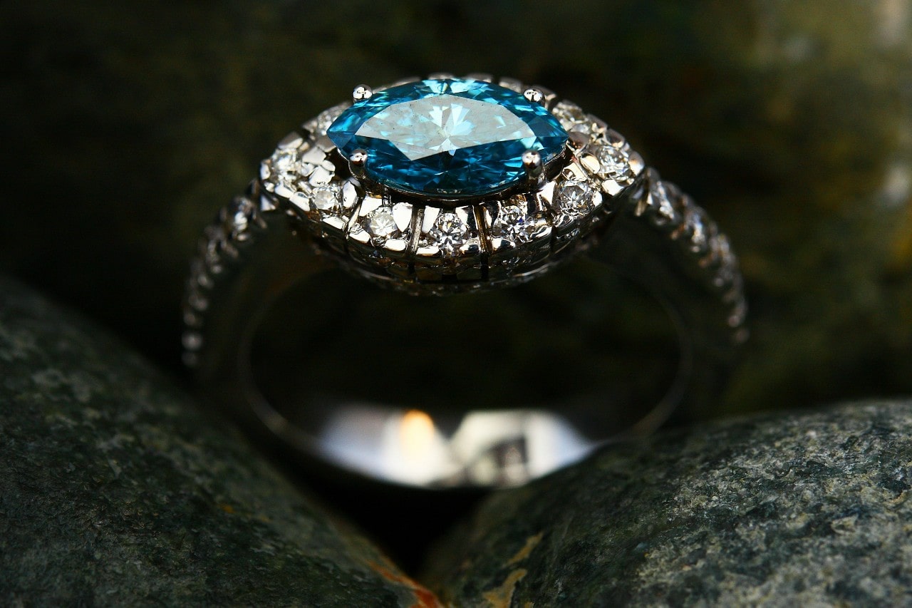 A close-up of an east-west oriented engagement ring with a blue center stone.