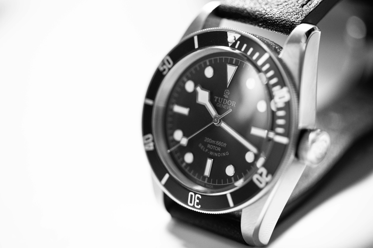 A black and white photo of a TUDOR wristwatch with black leather strap