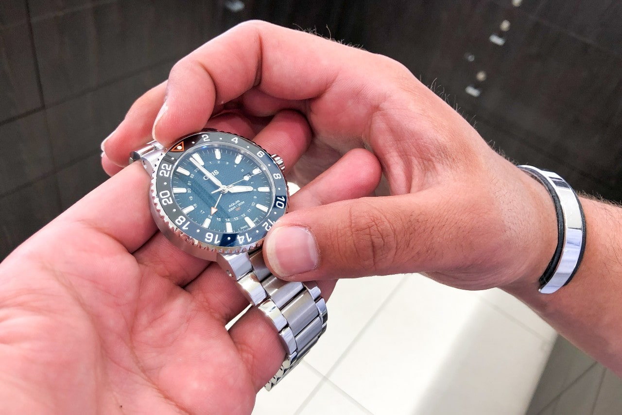 A close up of hands holding an Oris wristwatch with blue dial and metallic bracelet