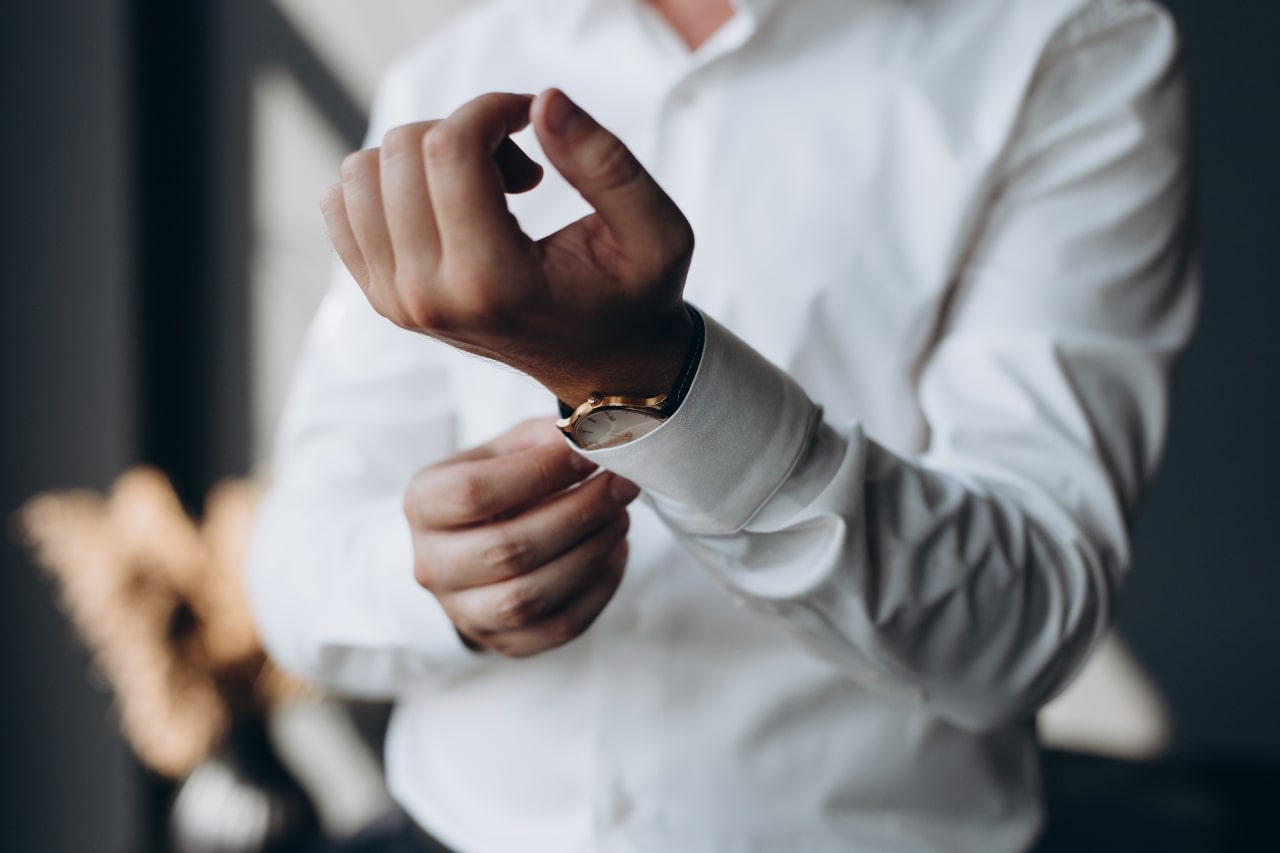 A man fastens the buttons on his sleeve, wearing a watch underneath the sleeve.