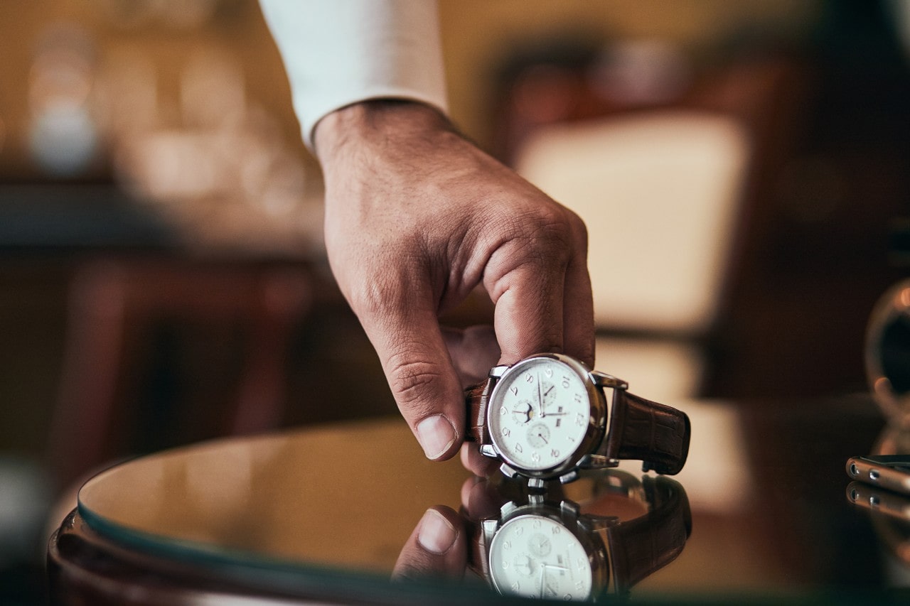 A man picks up his watch off of a glass coffee table.